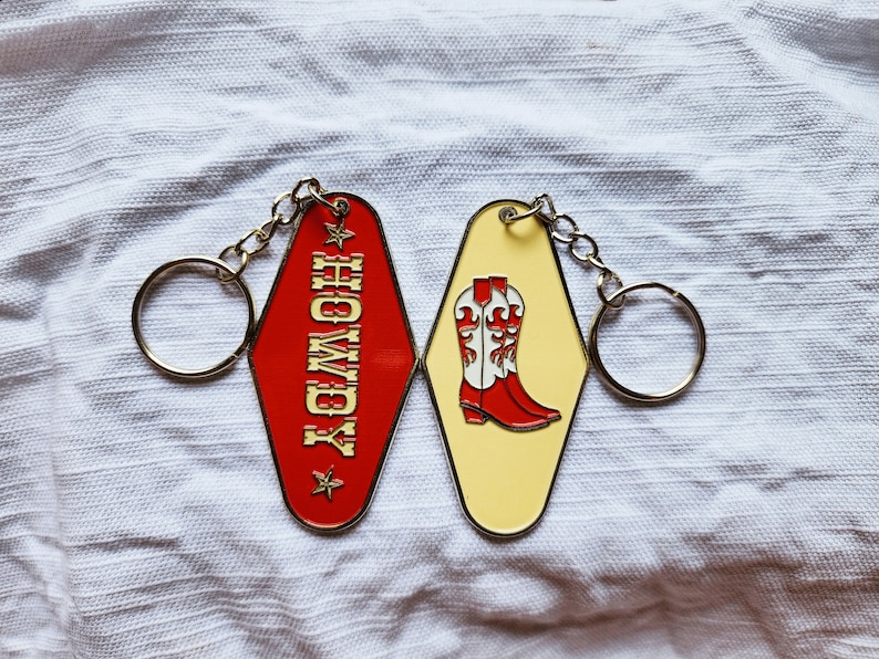 May include: A red and yellow metal keychain with a motel key tag that says "Howdy" and a second key tag with a pair of red cowboy boots with white accents.