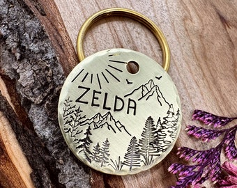 Könnte beinhalten: Ein Messing-Hundeanhänger mit einer Bergszene und dem eingravierten Namen "ZELDA". Der Anhänger ist an einem Schlüsselring befestigt.