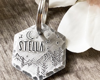 Könnte beinhalten: Silberner sechseckiger Haustieranhänger mit einem Design aus Gebirgskette, Mond und Sternen. Der Anhänger ist mit dem Namen "STELLA" graviert.