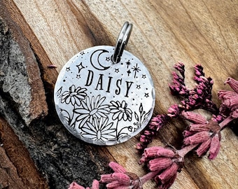 May include: Silver dog tag with a moon, stars, and daisies engraved on it. The tag says "DAISY" on it.