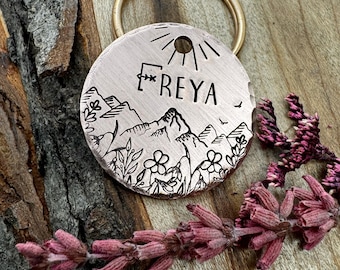 Könnte beinhalten: Ein kupferner Hundemarken mit einer Bergszene und dem eingravierten Namen "FREYA". Die Marke hat einen goldenen Ring.
