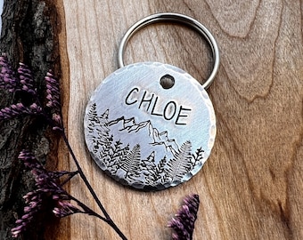 Può includere: Un'etichetta per cani in argento con un design di montagna e foresta e il nome Chloe inciso su di essa.