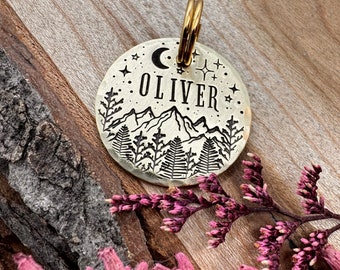 May include: A brass dog tag with a mountain scene, a crescent moon, and stars. The tag is engraved with the name "OLIVER".