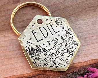 May include: A gold-toned hexagonal pet tag with a black engraved design. The tag features a moon, stars, trees, and a whale jumping out of the water. The name "EDIE" is engraved on the tag.