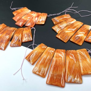 May include: A set of six orange and white agate gemstone beads with a wood-grain pattern. The beads are strung on a thin pink cord.