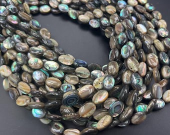 Peut inclure: Gros plan sur un tas de perles ovales en coquillage d'ormeau. Les perles présentent un mélange de couleurs, dont des bleus, verts et bruns irisés. Les perles lisses et polies reflètent la lumière.
