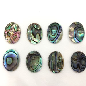Puede incluir: Ocho piezas ovaladas de concha de abulón con colores iridiscentes verdes, azules y morados. Las conchas tienen un patrón natural y orgánico.