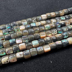 May include: Strands of square-shaped beads in shades of gray, brown, and iridescent colors. The beads have a polished, smooth surface and are strung together. The beads are likely made of natural materials and are suitable for jewelry making.