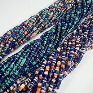 May include: Multiple strands of small, flat, circular disc beads arranged in long, parallel rows. The beads feature a vibrant color palette including deep royal blue, turquoise, white, and orange, creating a repeating, multi-colored pattern.