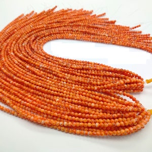 May include: A strand of orange coral beads, with a speckled white pattern, strung on clear thread. The beads are round and uniform in size.