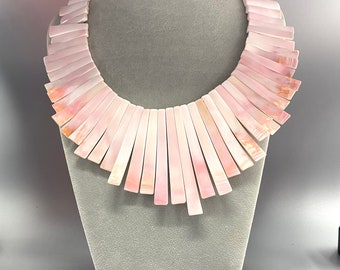 May include: A pink shell necklace with a fan-shaped design. The necklace is made of many individual shell pieces that are arranged in a graduated pattern.