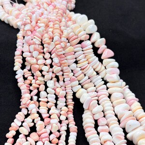May include: Multiple strands of small, irregular, tumbled beads in shades of soft pink, peach, and creamy white. The beads have a smooth, polished finish and are strung together, creating a cascading arrangement of light-colored, organic-shaped stones.