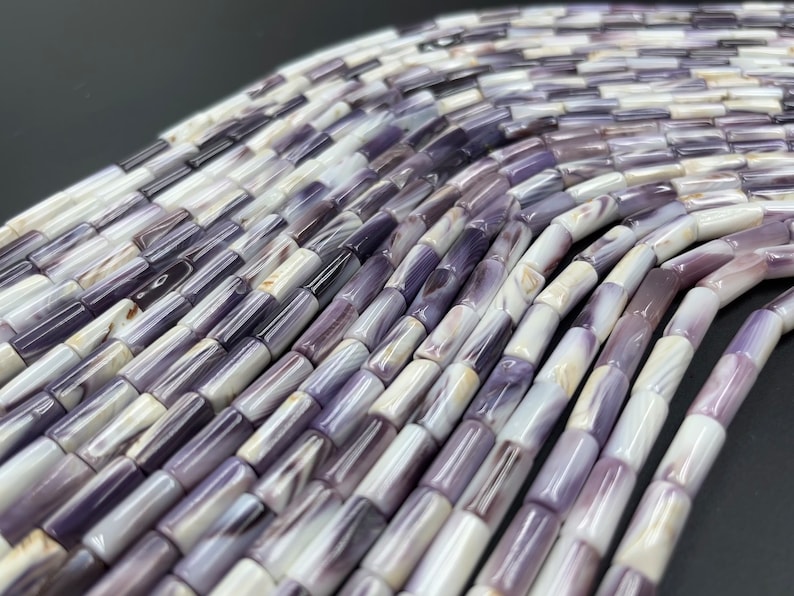 May include: A strand of purple and white shell beads, each bead is a cylinder shape.