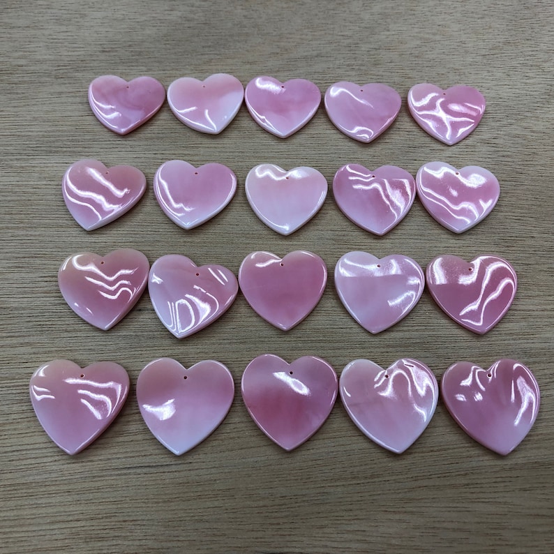 May include: Twenty pink heart-shaped shell charms with a hole at the top for stringing or attaching to jewelry.
