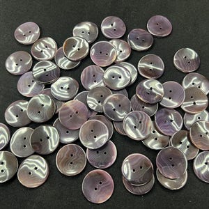 Pode incluir: Um conjunto de botões redondos iridescentes, com dois ou quatro furos. Os botões apresentam um padrão perolado e rodopiante em tons de cinza, roxo e prata. Estes botões decorativos são adequados para projetos de costura e artesanato.