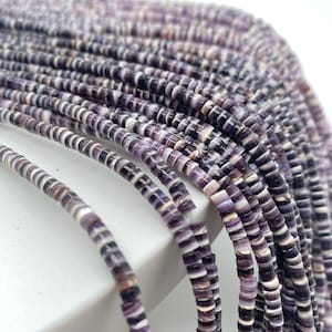 May include: A strand of purple and white shell beads. The beads are small and round, and they are strung together on a thin thread.