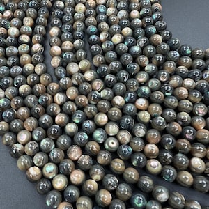 May include: A close-up shot of strands of round beads. The beads are a mix of dark gray, brown, and iridescent colors. The beads have a smooth, polished surface and are strung together. The beads are likely used for jewelry making.