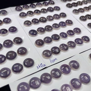 May include: A close-up of a collection of round, purple and white shell cabochons, arranged on white cards. The cards are labeled with the number of pieces and the size of the cabochons, which are 10mm and 36 pieces.