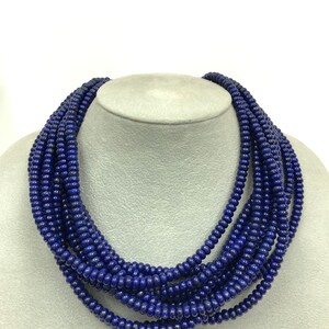May include: A multi-strand necklace composed of small, round, deep blue beads. The necklace is displayed on a gray mannequin head, showcasing its layered design and rich color. The beads appear to be uniform in size and shape.