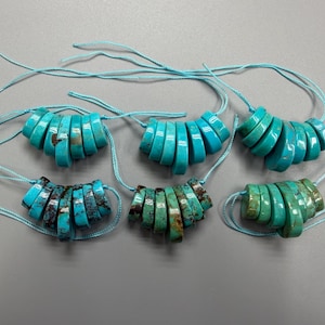 May include: Six strands of turquoise gemstone beads, each composed of graduated, circular slices. The beads vary in shades of blue and green, with some showing brown matrix patterns. Each strand is strung on a light blue cord.