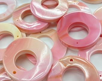 May include: A collection of pink and white iridescent shell rings with a smooth, polished finish. The rings have a large hole in the centre, making them suitable for crafting projects.
