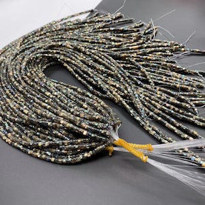May include: A bundle of iridescent black and gold square beads, strung on thin white thread. The beads are arranged in a loose, flowing pattern, and the ends of the thread are tied together.