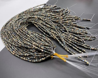 Peut inclure: Un paquet de perles carrées noires et dorées irisées, enfilées sur un fil blanc fin. Les perles sont disposées en un motif lâche et fluide, et les extrémités du fil sont nouées ensemble.