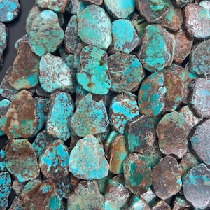 Puede incluir: Una colección de piedras de turquesa planas e irregulares con una vibrante paleta de colores azul verdoso y vetas de matriz de color marrón oscuro. Cada piedra presenta una forma orgánica única con una superficie pulida y variaciones naturales.