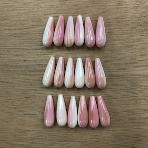 Könnte beinhalten: Achtzehn einzelne künstliche Fingernägel, angeordnet in drei horizontalen Reihen. Jeder Nagel hat eine glänzende, längliche Mandelform mit einer marmorierten Mischung aus zartem Rosa und Cremeweiß für ein glattes Finish.