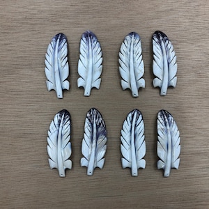 Op de afbeelding: Acht witte en paarse schelpverencharms met een gesneden ontwerp.