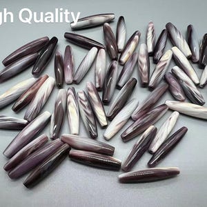 May include: A collection of approximately 30 purple and white shell beads. The beads are oval shaped and have a natural, organic look.