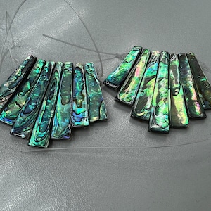 Puede incluir: Dos juegos de colgantes de concha de abulón verde iridiscente, cada juego consta de siete piezas dispuestas en forma de abanico.