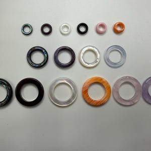 May include: A collection of various-sized, circular jewelry pieces. The pieces are in a range of colors, including black, pink, orange, and purple. Some have iridescent or marbled patterns. The jewelry is likely for ear piercings or other body modifications.