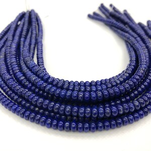 May include: Close-up of several strands of dark blue beads. The beads are small, round, and have a glossy finish. The strands are arranged in a curved shape, with the ends of the strands visible at the top. The background is white.