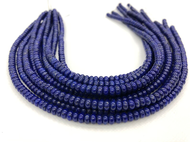 May include: Close-up of several strands of dark blue beads. The beads are small, round, and have a glossy finish. The strands are arranged in a curved shape, with the ends of the strands visible at the top. The background is white.