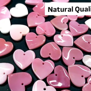 May include: A collection of pink and white heart-shaped shell charms with a hole for stringing. The charms are natural and have a glossy finish. The text "Natural Quality" is visible in the image.