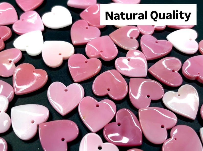 May include: A collection of pink and white heart-shaped shell charms with a hole for stringing. The charms are natural and have a glossy finish. The text "Natural Quality" is visible in the image.