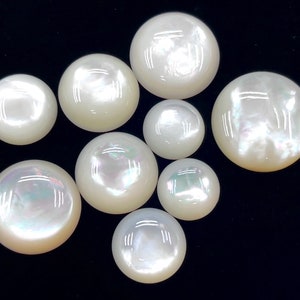 May include: A collection of nine white mother of pearl cabochons of varying sizes. The cabochons are smooth and have a pearlescent sheen.
