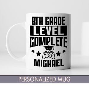 May include: White ceramic mug with black text that reads "8th Grade Level Complete" with a graduation cap and a video game controller graphic. The name "Michael" is printed below the graphic. "Personalized Mug" is printed below the image.