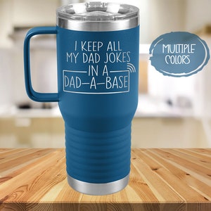 May include: A blue stainless steel travel mug with a handle. The mug has a white inscription that reads "I keep all my dad jokes in a dad-a-base" with a wifi symbol. The mug is on a wooden surface. The text "MULTIPLE COLORS" is in a circle in the upper right corner of the image.