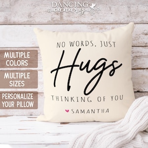 May include: Cream-colored decorative pillow with the words "NO WORDS, JUST Hugs" in black script. Below, it reads "THINKING OF YOU" and "SAMANTHA" with a pink heart. The pillow is on a white wooden surface.