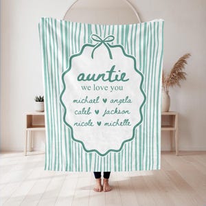 May include: A teal and white striped throw blanket featuring a central scalloped frame with a bow at the top. The text reads "auntie we love you" followed by the names "michael", "angela", "caleb", "jackson", "nicole", and "michelle" with hearts.