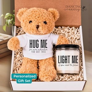May include: A personalized gift set featuring a tan teddy bear wearing a white t-shirt with the text "HUG ME" and a candle with the text "LIGHT ME". The set is presented in a gift box.