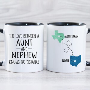 May include: Two white coffee mugs with black handles and black rims. One mug says "The love between an aunt and nephew knows no distance". The other mug has a map of Texas and Ohio with a heart in each state and the text "Aunt Sarah" and "Noah".