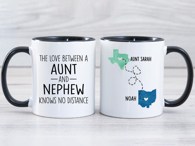 May include: Two white coffee mugs with black handles and black rims. One mug says "The love between an aunt and nephew knows no distance". The other mug has a map of Texas and Ohio with a heart in each state and the text "Aunt Sarah" and "Noah".