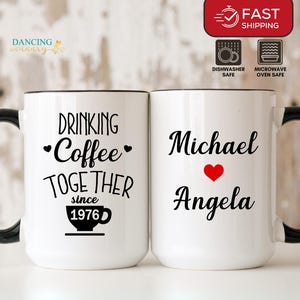 May include: Two white ceramic mugs with black handles and rims. One mug reads "Drinking Coffee Together since 1976". The other mug has the names "Michael" and "Angela" with a red heart. Dishwasher and microwave safe.