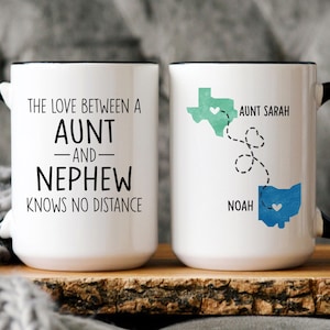 May include: Two white coffee mugs with black handles. One mug has the text "The love between an aunt and nephew knows no distance". The other mug has a map of the United States with a heart in Texas and a map of Ohio with a heart in Ohio. The text "Aunt Sarah" is above Texas and "Noah" is below Ohio.