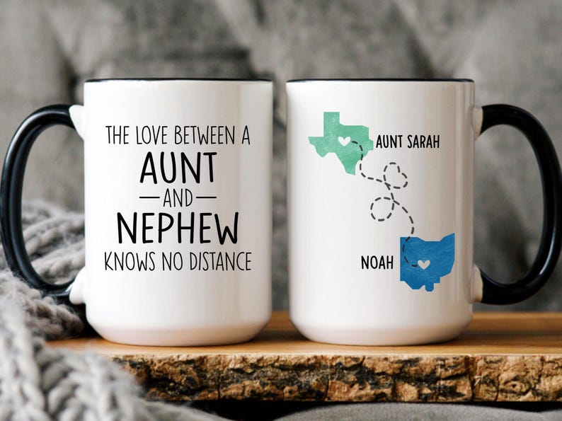 May include: Two white coffee mugs with black handles. One mug has the text "The love between an aunt and nephew knows no distance". The other mug has a map of the United States with a heart in Texas and a map of Ohio with a heart in Ohio. The text "Aunt Sarah" is above Texas and "Noah" is below Ohio.