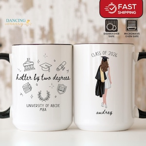 Peut inclure: Mug en céramique blanche avec anse et bord noirs. Un côté affiche le texte "hotter by two degrees" avec des illustrations sur le thème de la remise de diplômes. L'autre côté affiche "Class of 2026" et une illustration de remise de diplôme.
