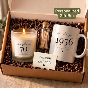 May include: A gift box containing a lit candle with a label reading 'chapter 70', a small glass bottle filled with wooden matches, a white ceramic mug printed with 'vintage 1956 angela' and a heart, and a card labeled 'custom gift note'.